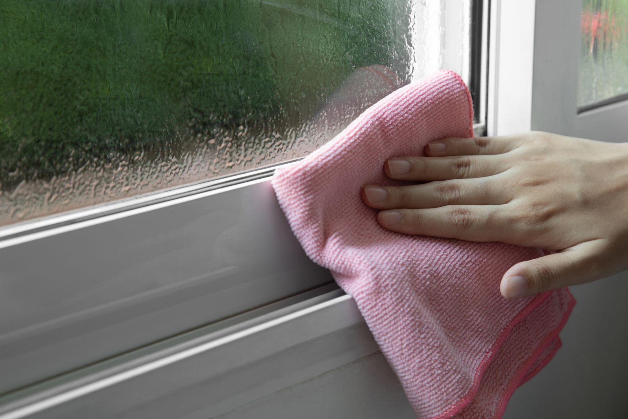 Hand uses folded up pink hand towel to wipe away moisture from window frame due to excess humidity