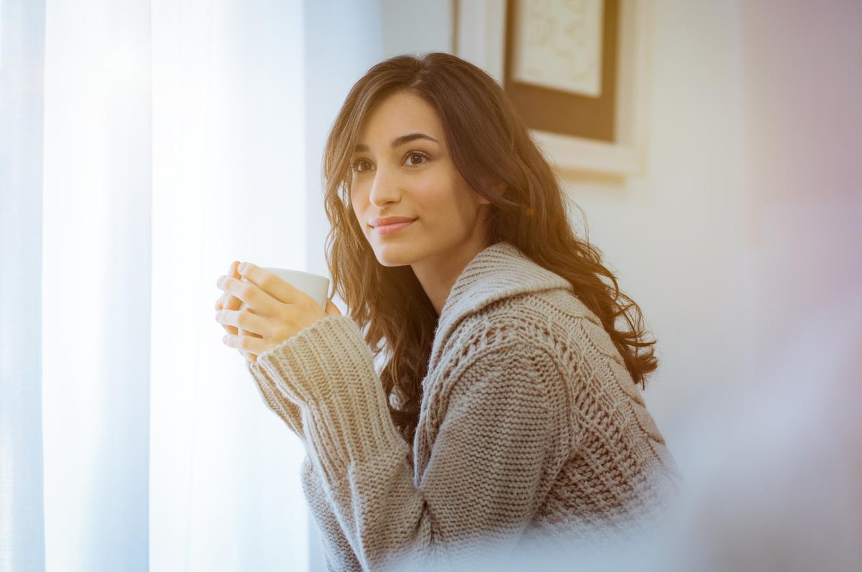 A young woman relaxing at home with a cup of coffee. 